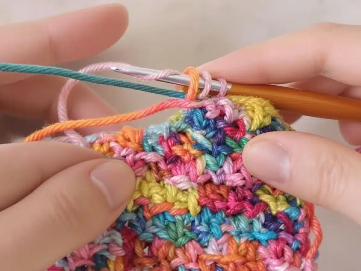 Hands crocheting a vibrant treble stitch with colorful yarn.